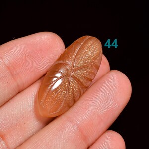 Peut inclure: Un cabochon de pierre de soleil sculpt&eacute; avec un motif de feuille. La pierre est de couleur orange clair avec des paillettes dor&eacute;es. Le cabochon mesure environ 2,5 cm de long et 1,5 cm de large. #44