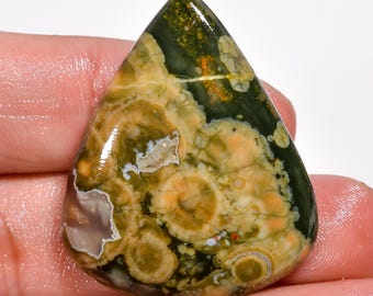 May include: A green, brown, and white ocean jasper cabochon with a unique, swirling pattern. The stone is smooth and polished, with a glossy finish.