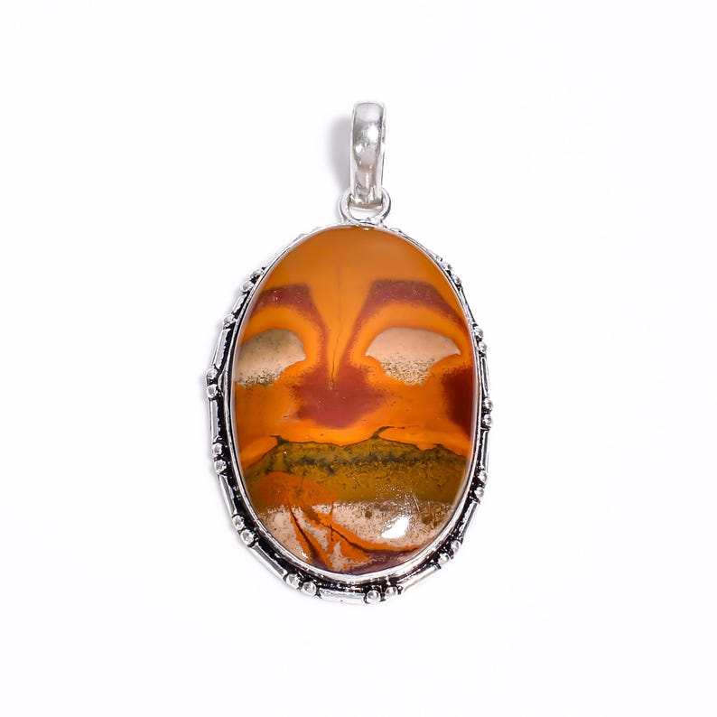 May include: Oval pendant with a silver-colored bail and decorative border. The pendant features a polished stone with a warm color palette of orange, brown, and cream, with a hint of green. The stone has a unique, natural pattern.