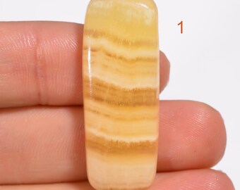Pode incluir: Um cabochão de ágata amarelo e branco, com formato retangular. A pedra tem uma superfície lisa e polida.