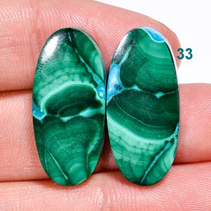 May include: Pair of oval-shaped green and blue malachite cabochons. The stones have a swirling pattern of green and blue.