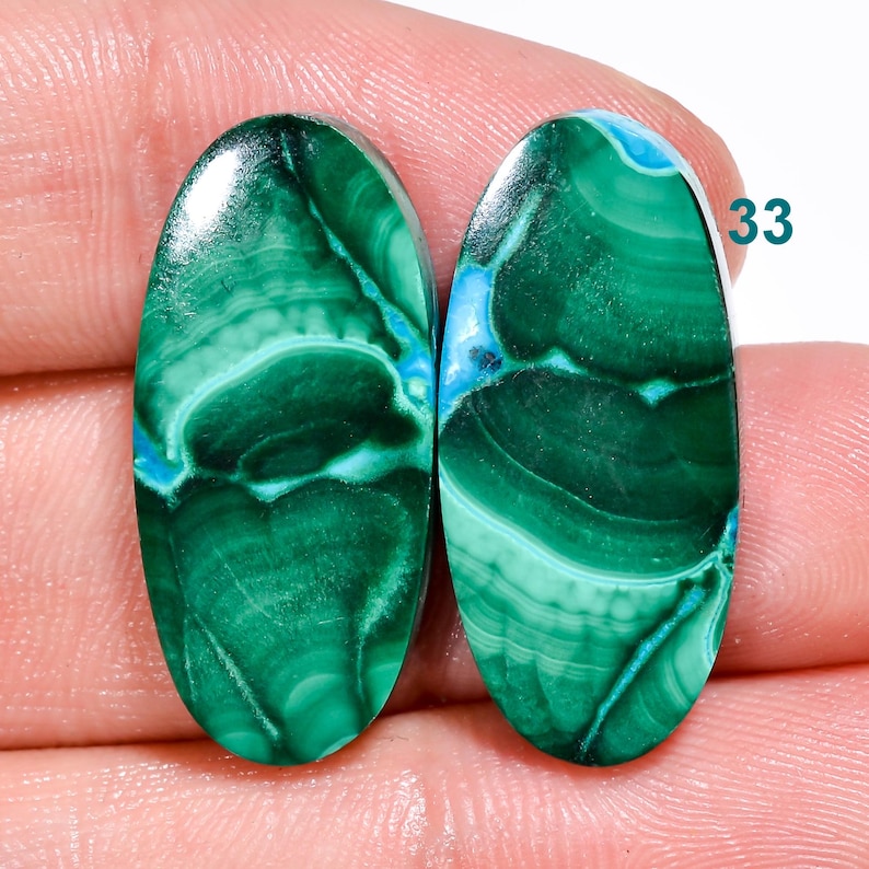 May include: Pair of oval-shaped green and blue malachite cabochons. The stones have a swirling pattern of green and blue.