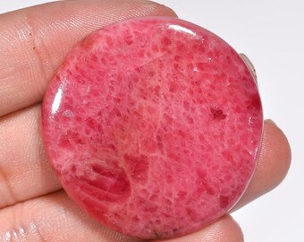 May include: A round, pink, polished gemstone with a smooth, textured surface. The stone has a natural, organic look.