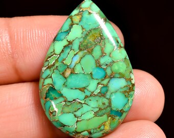 May include: A teardrop-shaped gemstone with a mosaic pattern of turquoise, teal, and green hues, interspersed with golden-brown matrix lines. The polished surface reflects light, highlighting the stone's natural variations. This gemstone is likely used in jewelry.