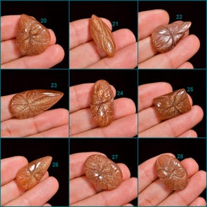 Peut inclure: Neuf cabochons de pierre de soleil sculpt&eacute;s de diff&eacute;rentes formes et tailles, notamment en forme de larme, ovale et rectangulaire. Les pierres sont de couleur brun rouge&acirc;tre chaud avec une finition chatoyante et iris&eacute;e.