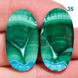 May include: Pair of oval-shaped green and blue gemstone cabochons with white veining. The cabochons are approximately 2.5 cm in length.
