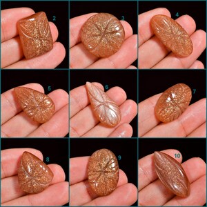 Peut inclure: Dix cabochons de pierre de soleil diff&eacute;rents, chacun avec un motif sculpt&eacute; unique. Les cabochons sont de formes et de tailles vari&eacute;es, allant de l'ovale &agrave; la goutte d'eau. Les pierres sont d'une couleur brun rouge&acirc;tre chaude avec un effet chatoyant et iris&eacute;.