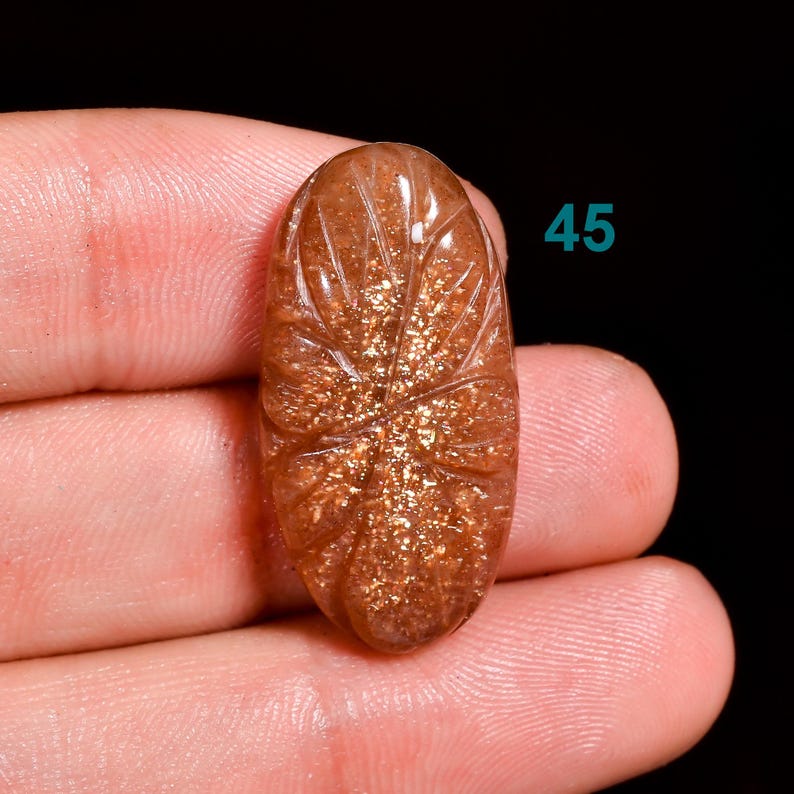 Peut inclure: Un cabochon ovale en pierre de soleil sculpt&eacute; avec une brillance dor&eacute;e et un motif de feuille. La pierre mesure environ 45 mm de long.