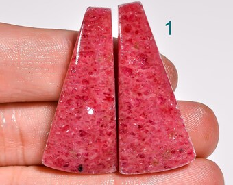 May include: Two polished, triangular-shaped gemstones with a vibrant pink hue. The stones have a textured surface and are displayed side-by-side. The number "1" is visible in the upper right corner. These gemstones are ideal for jewelry making or collecting.