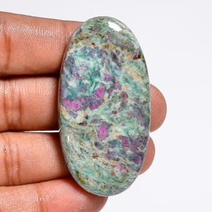 May include: An oval-shaped gemstone with a mix of colors. The stone features a base of light green and white, with patches of vibrant pink and darker green. The polished surface reflects light, highlighting the stone's natural patterns and textures.