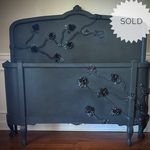Puede incluir: Un marco de cama gris oscuro con adornos florales. El cabecero y el pie de cama están adornados con rosas y vides en relieve. La palabra "SOLD" se muestra en el cabecero.
