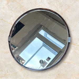 Può includere: Uno specchio rotondo con cornice nera e bordo bisellato. Lo specchio riflette una stanza con una finestra e altri oggetti.