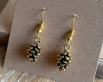 May include: A pair of gold-tone earrings with a pine cone design. The earrings are hanging on a brown card.