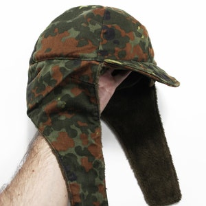 May include: A camouflage-patterned winter hat with a long ear flap. The hat is made of a thick, durable fabric and has a fleece lining for warmth.