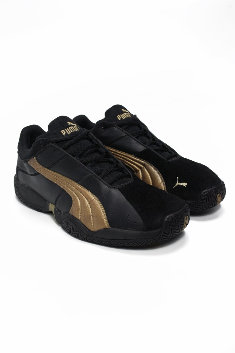 K&ouml;nnte beinhalten: Schwarze und goldene Puma-Sneaker mit Wildlederspitze und schwarzer Gummisohle.