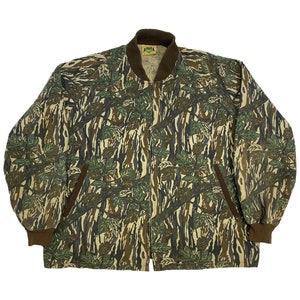 May include: A green, brown, and tan camouflage jacket with a zipper closure. The jacket has a ribbed collar and cuffs.