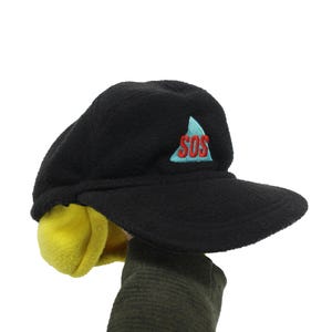 May include: Black fleece hat with a yellow ear flap and a blue and red embroidered triangle with the word "SOS" inside.