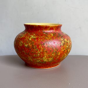 Puede incluir: Un jarrón redondo de cerámica con una superficie texturizada. El jarrón presenta una vibrante paleta de colores rojo, amarillo y verde. El borde interior es amarillo. El jarrón es un objeto decorativo.