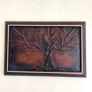 Puede incluir: Una pieza de arte de pared enmarcada que presenta un árbol de cuero marrón en relieve sobre un fondo marrón oscuro.
