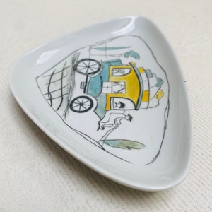 Puede incluir: Un plato triangular de cerámica blanca con un dibujo en blanco y negro de un carruaje tirado por un caballo. El carruaje es amarillo y azul con ruedas negras. El plato es de diseño vintage.