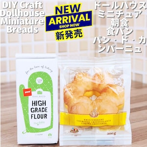 May include: A white bag of high-grade flour and a clear bag of miniature breads. The flour bag has green accents and text that reads "High Grade Flour". The bread bag has a yellow label and contains several golden-brown baked goods, weighing 300g.