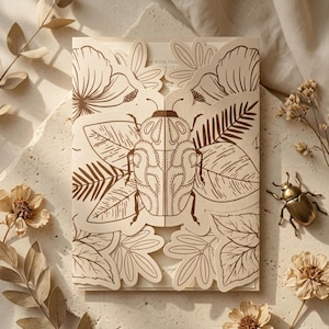 Peut inclure: Une carte d'invitation crème à ouverture centrale présentant une illustration au trait marron d'un scarabée centrée sur les panneaux avant, entourée de motifs botaniques complexes de feuilles et de fleurs. La carte est fermée.
