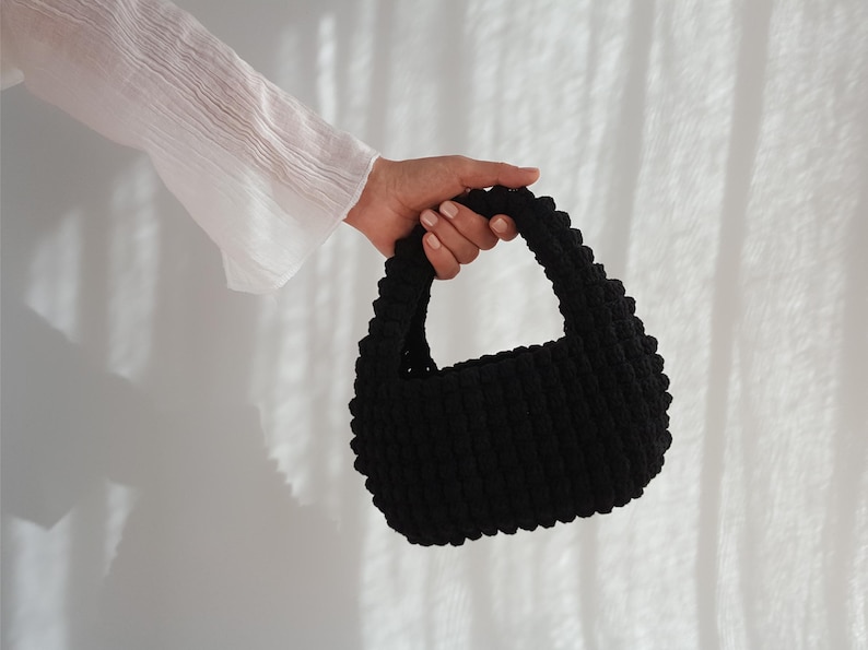 K&ouml;nnte beinhalten: Eine schwarze, geh&auml;kelte Handtasche mit abgerundeter Form und einem einzigen Henkel.
