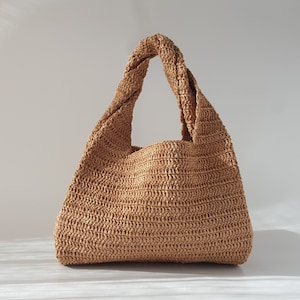 K&ouml;nnte beinhalten: Eine braune geflochtene Strohtasche mit einem verdrehten Henkel.