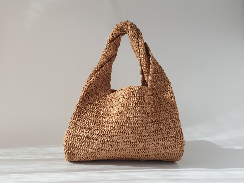 K&ouml;nnte beinhalten: Eine braune geflochtene Strohtasche mit einem verdrehten Henkel.