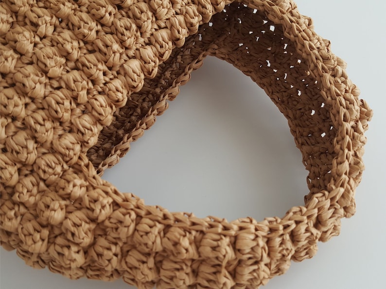 K&ouml;nnte beinhalten: Nahaufnahme einer braunen geflochtenen Strohtasche mit einem abgerundeten Henkel. Die Tasche ist aus dicht geflochtenem Stroh mit einer strukturierten Oberfl&auml;che.