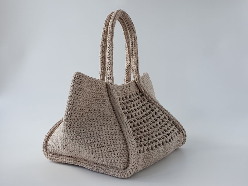 Op de afbeelding: Een beige gehaakte tote bag met een geweven patroon aan de ene kant. De tas heeft twee dikke gehaakte handvatten.