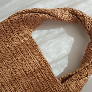 K&ouml;nnte beinhalten: Eine braune gewebte Tragetasche mit einem geknoteten Henkel. Die Tasche ist aus einem strukturierten Material gefertigt und hat einen l&auml;ssigen, entspannten Stil.