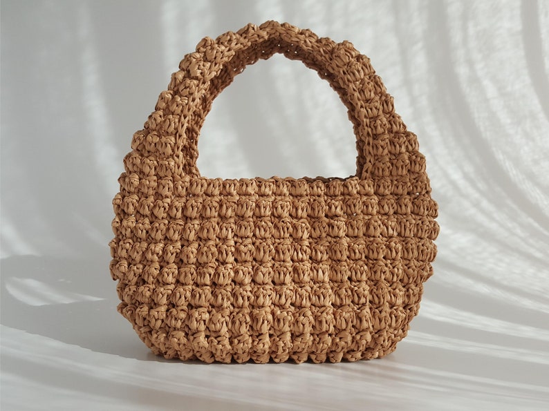 K&ouml;nnte beinhalten: Eine kleine, braune, geflochtene Strohtasche mit einem einzigen Henkel oben.