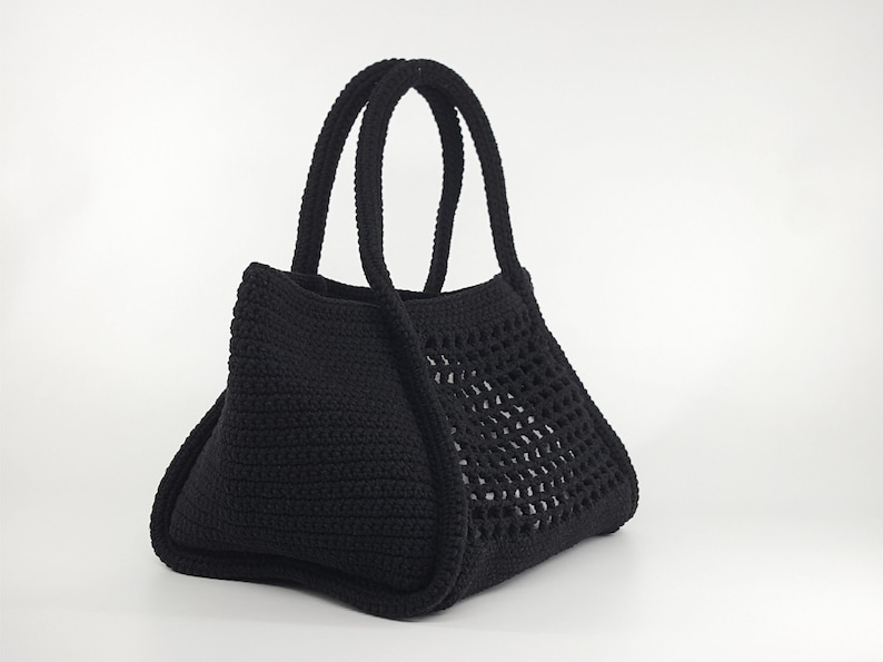Op de afbeelding: Een zwarte gehaakte tote bag met een gaasontwerp aan de voorkant. De tas heeft twee handvatten.