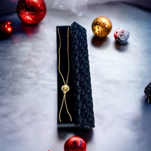 May include: A gold necklace with a round pendant featuring a clear stone surrounded by smaller stones, in a black velvet box with a floral pattern.