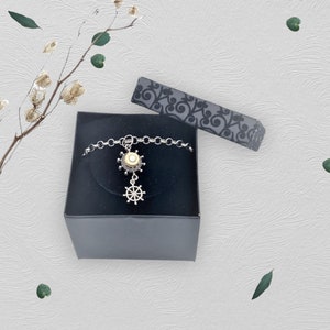 May include: A silver bracelet with a gold and white ship's wheel charm. The bracelet is in a black gift box.