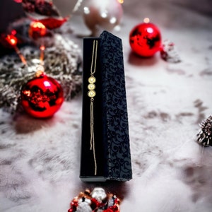 May include: A gold necklace with three round pendants in a black velvet jewelry box. The box is decorated with a floral pattern.