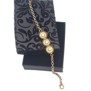 May include: Gold chain bracelet with three round charms featuring clear rhinestones. The bracelet is in a black velvet box.