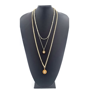May include: A gold layered necklace with three chains and two round pendants with clear stones.