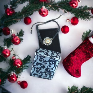 May include: A black and silver bracelet with a round charm, displayed on a blue and black patterned box. The bracelet is surrounded by red Christmas ornaments and a red stocking.