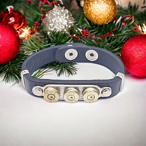 May include: A dark blue leather bracelet with silver accents and three brass bullet casings. The bracelet is on a white surface.