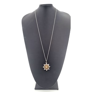 May include: A silver chain necklace with a round pendant featuring a brown and gold design. The pendant has a circular shape with a raised center and a silver rim.