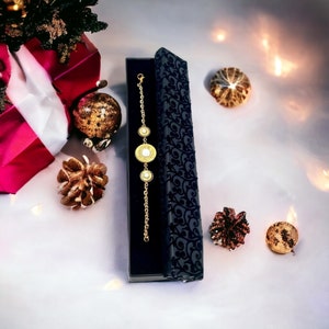 May include: A gold bracelet with three round charms, each with a white center, in a black velvet box. The box is decorated with a floral pattern.