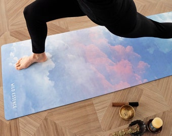 May include: A person doing yoga on a blue and pink yoga mat with a cloud design. The mat has the words "Wild Essence" printed on it.