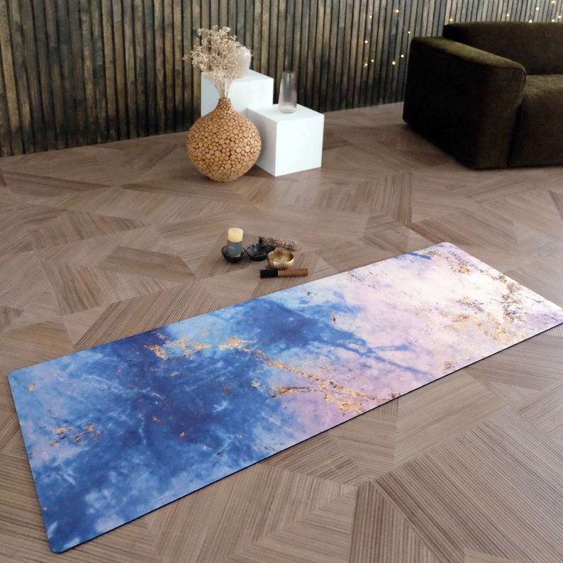 Op de afbeelding: Een blauwe en roze yogamat met gouden accenten en een marmerachtig patroon. De mat ligt op een houten vloer.
