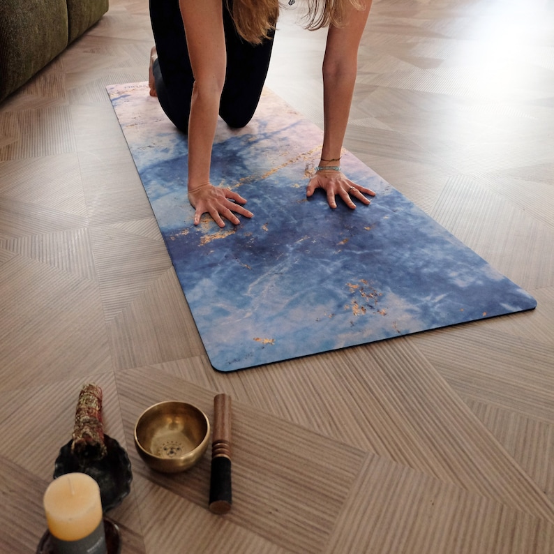 Op de afbeelding: Een blauwe en gouden yogamat met een marmerachtig patroon. De mat ligt op een houten vloer.