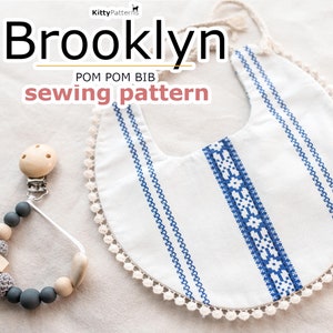 Może przedstawiać: Biały bawełniany śliniak dla niemowląt z niebieskim haftowanym wykończeniem i białym wykończeniem z pomponów. Śliniak nazywa się "Brooklyn Pom Pom Bib Sewing Pattern".
