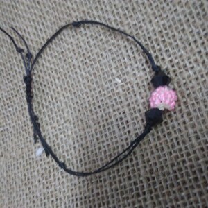 Könnte beinhalten: Ein schwarzes Armband aus Schnur mit einem rosa und schwarzen Perlenanhänger.