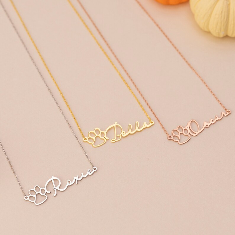 May include: Three gold necklaces with paw print charms and personalized names. The names are "Rexie", "Bella", and "Oscar".