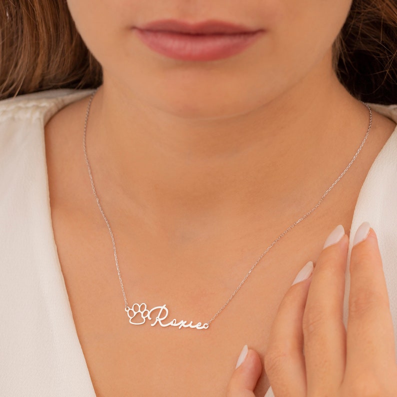 May include: Silver necklace with a paw print charm and the name "Roxie" written in cursive.